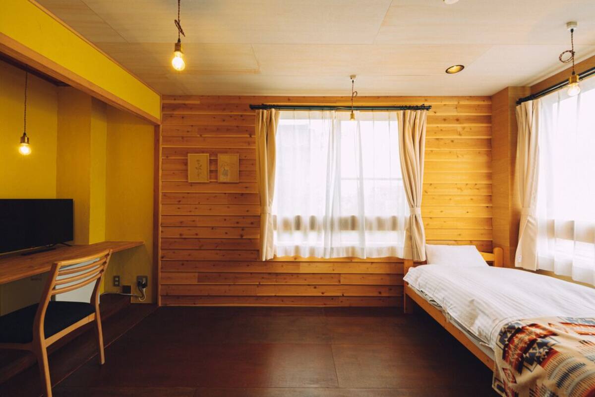 A room with a wooden wall, a bed, a desk with a chair, and a TV.
