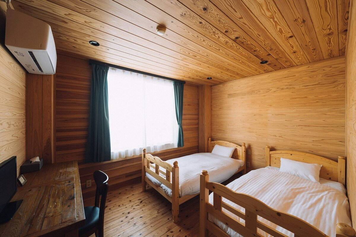 A wooden cabin room with two beds, a table, and a chair.