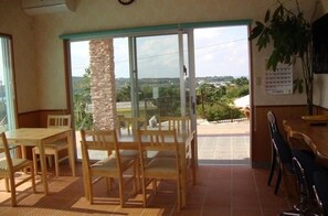 A room with a dining table and chairs, a stone pillar, and a view through a glass door. - Pension Nami (Motobu)