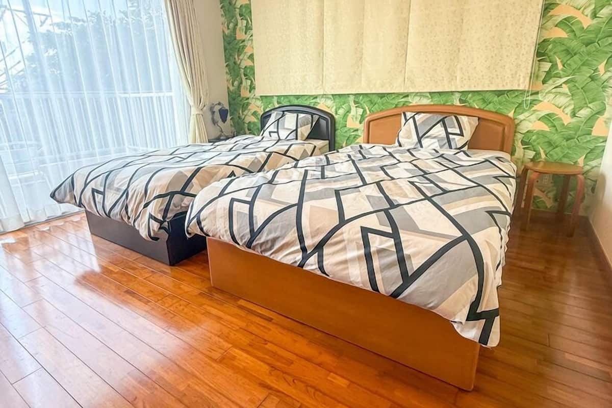 Parivuode, jossa on geometrisesti kuvioitu peitto, puinen pääty ja suuri ikkuna, jossa on läpikuultavat verhot.