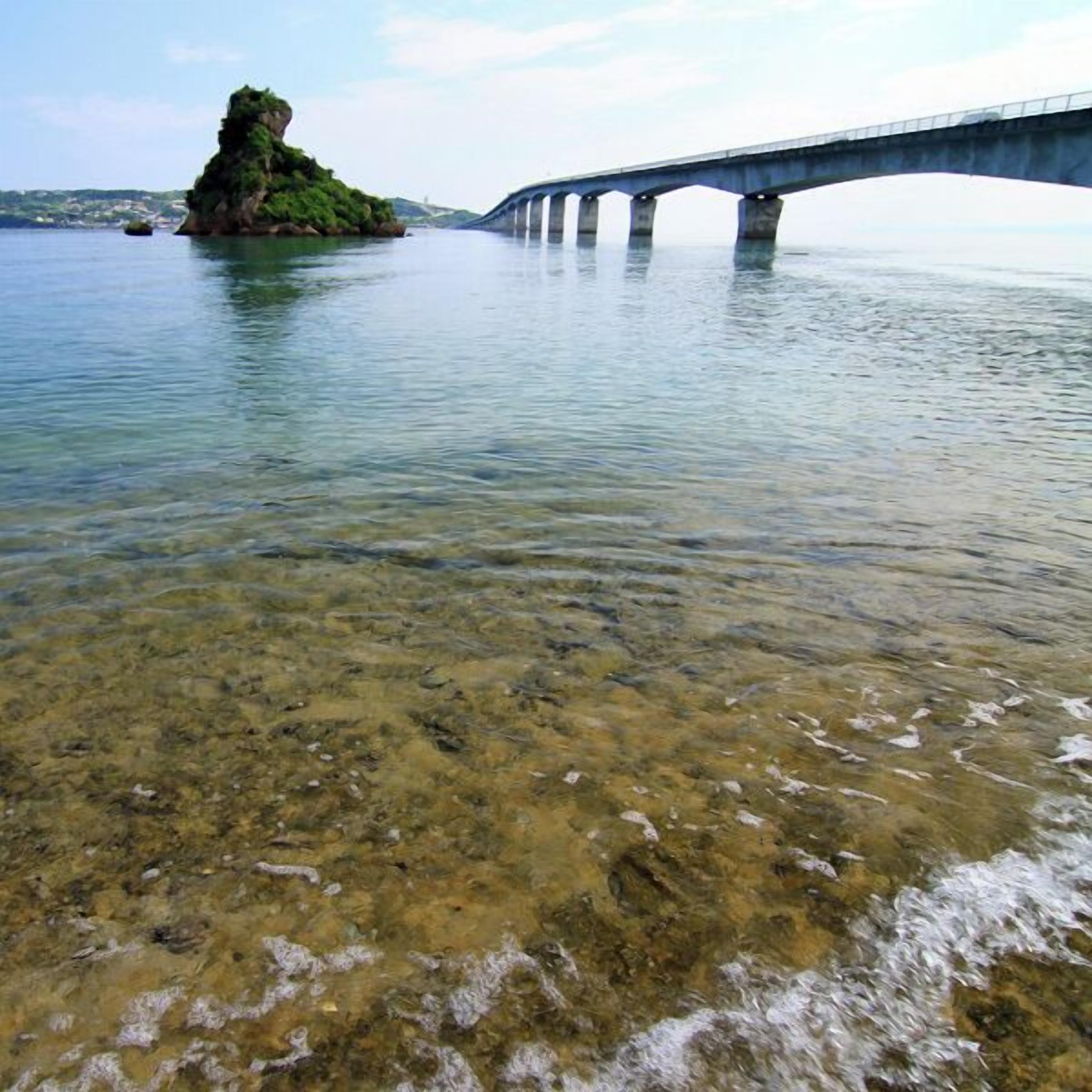 A bridge over water with clear shallow areas and a rocky island.