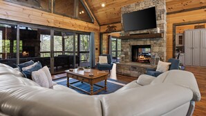 Ein großzügiges Wohnzimmer mit Kamin aus Stein, Ledersofas und einem großen, an der Wand befestigten Fernseher.