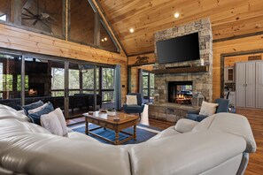Ein großzügiges Wohnzimmer mit Kamin aus Stein, Ledersofas und einem großen, an der Wand befestigten Fernseher.