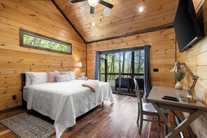 A wooden cabin bedroom with a bed, desk, and large windows. - Whiskey Bent, Mineral Bluff, GA (Mineral Bluff)
