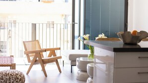 Un apartamento moderno con balcón, un sofá, una silla de madera, una zona de cocina y vistas a la ciudad.