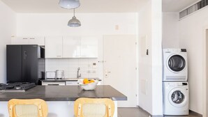 Una cocina moderna con un refrigerador negro, gabinetes blancos, una encimera gris y una lavadora.