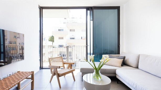 Una sala de estar moderna con un sofá, un sillón, una mesa de centro y un televisor en la pared.