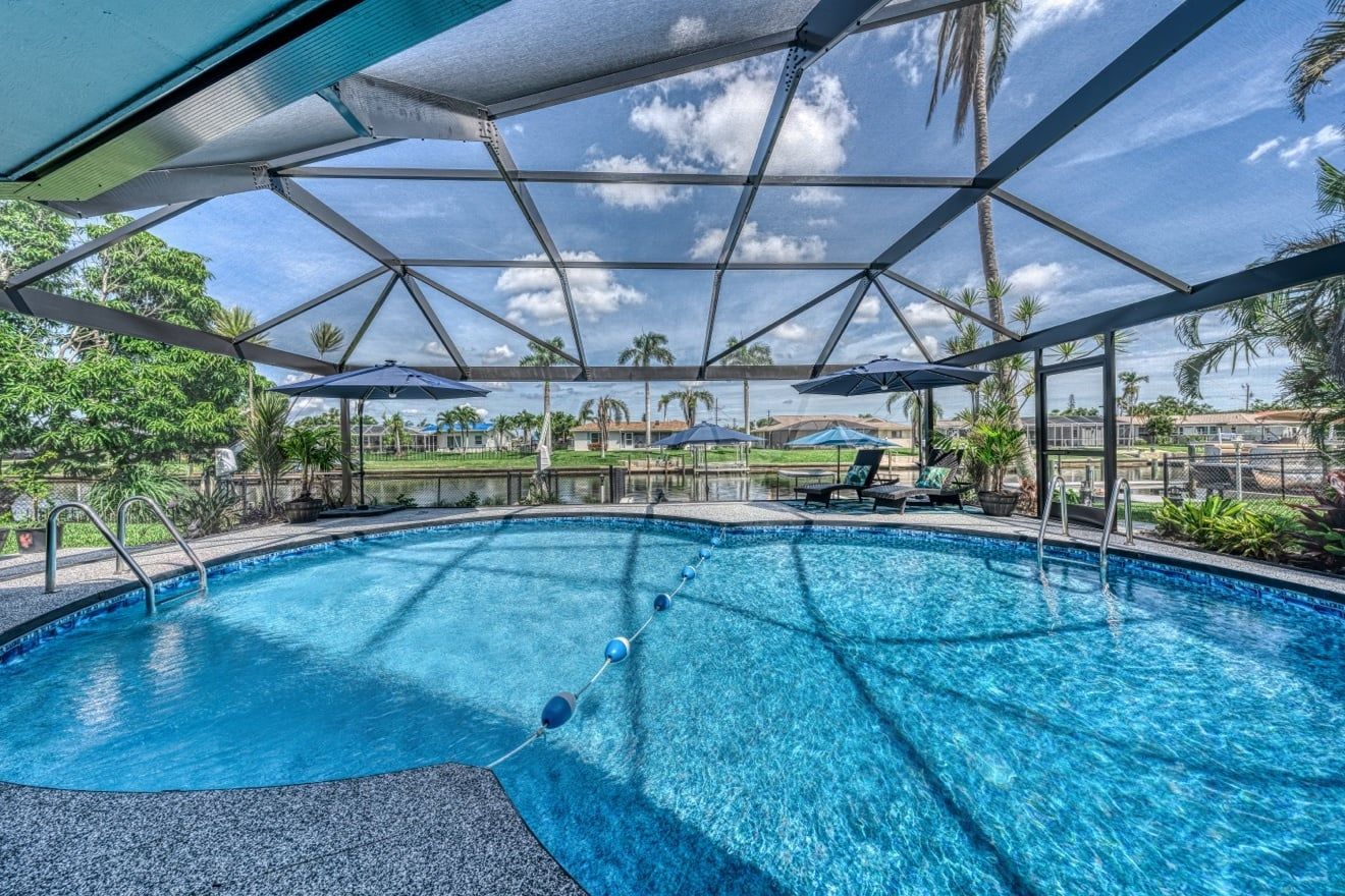 A swimming pool with a clear view of the surrounding landscape, including palm trees and a distant body of water.