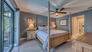A bedroom with a four-poster bed, bedside lamps, a ceiling fan, and a view through a sliding glass door.