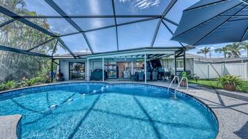 A swimming pool with a covered area, surrounded by a fence, and palm trees in the background.