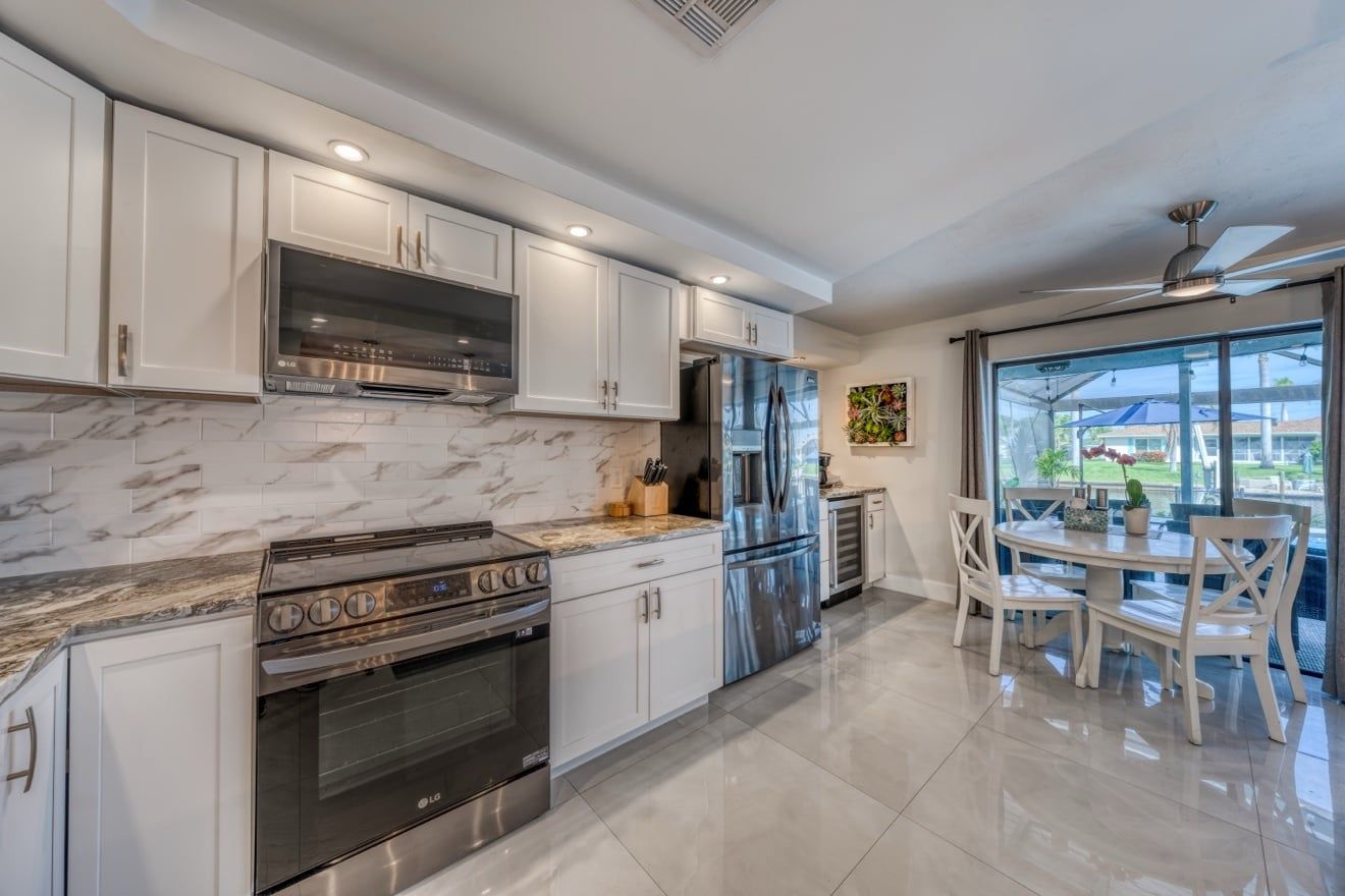 A modern kitchen with white cabinetry, stainless steel appliances, and a dining area with a table and chairs.