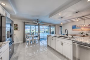 A modern kitchen with a large island, stainless steel appliances, and a view through glass doors to the outdoors. - Waterfront Luxury Micro Resort Heated Salt Pool 4 Bedroom Home (Cape Coral)