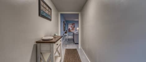 A hallway with a wooden table, a rug, and a kitchen in the background.