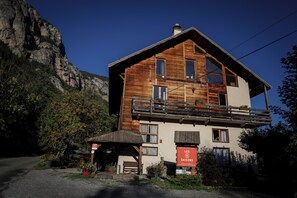 Un edificio in legno con un balcone, un cartello con la scritta 'LES SAISONS' e montagne sullo sfondo.