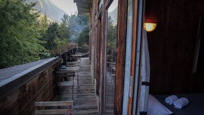 A wooden deck with tables and benches, a bed with pillows, and a view of a forested area. - Hotel les 5 saisons (Freissinières)