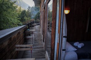 Un pontile in legno con tavoli e panche, un letto con cuscini e vista su una zona boschiva.
