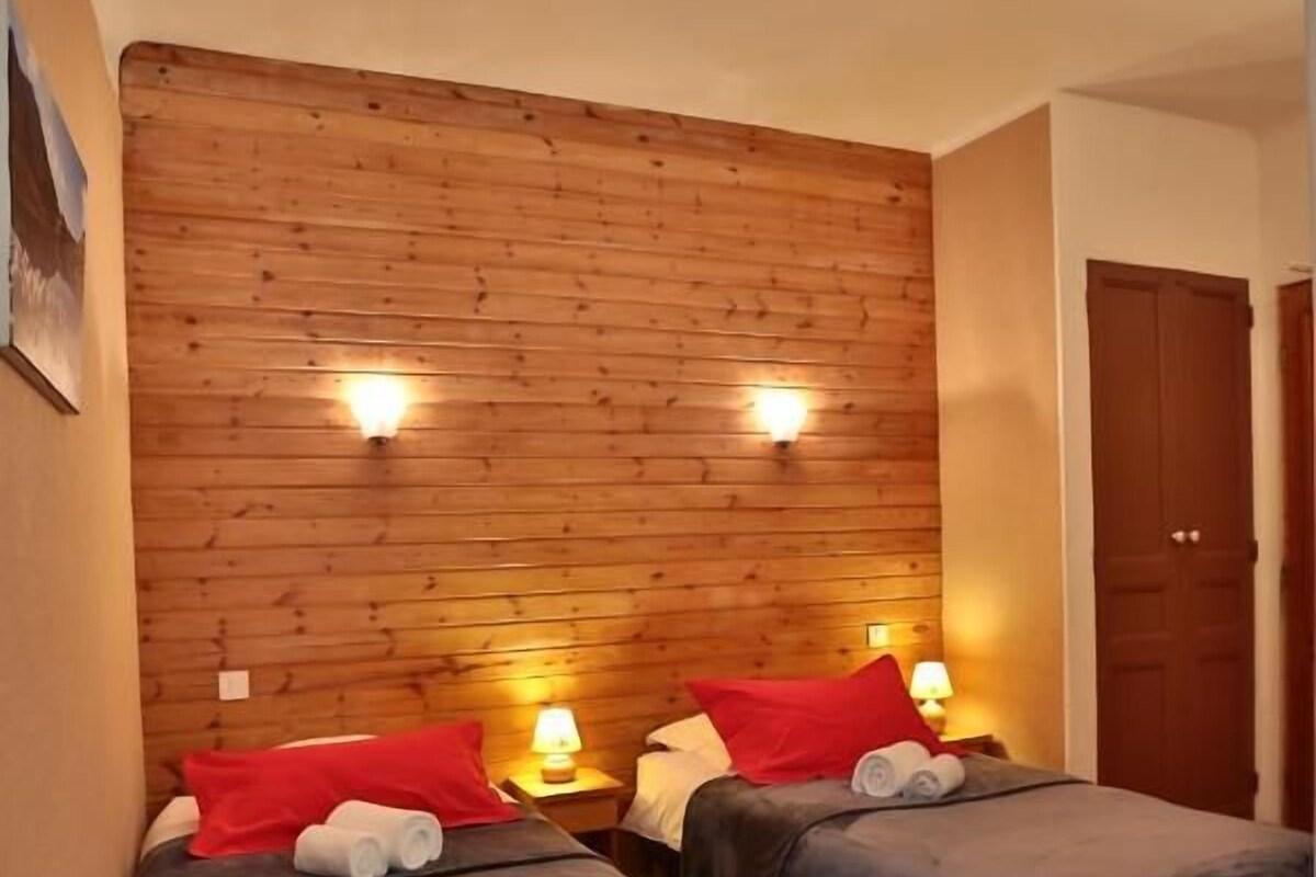 Una habitación con dos camas, cabecero de madera, luces fijadas en la pared y una puerta.