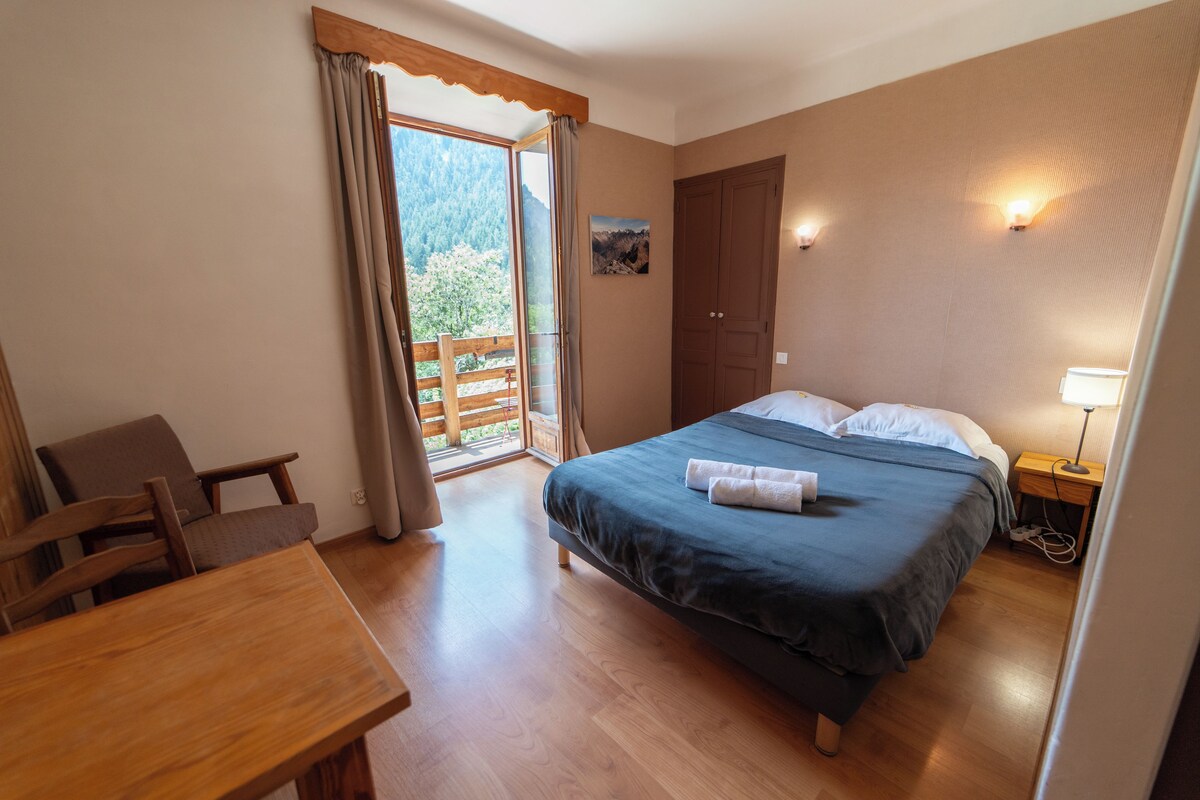 Un dormitorio con cama, escritorio, silla, armario y vistas al exterior.