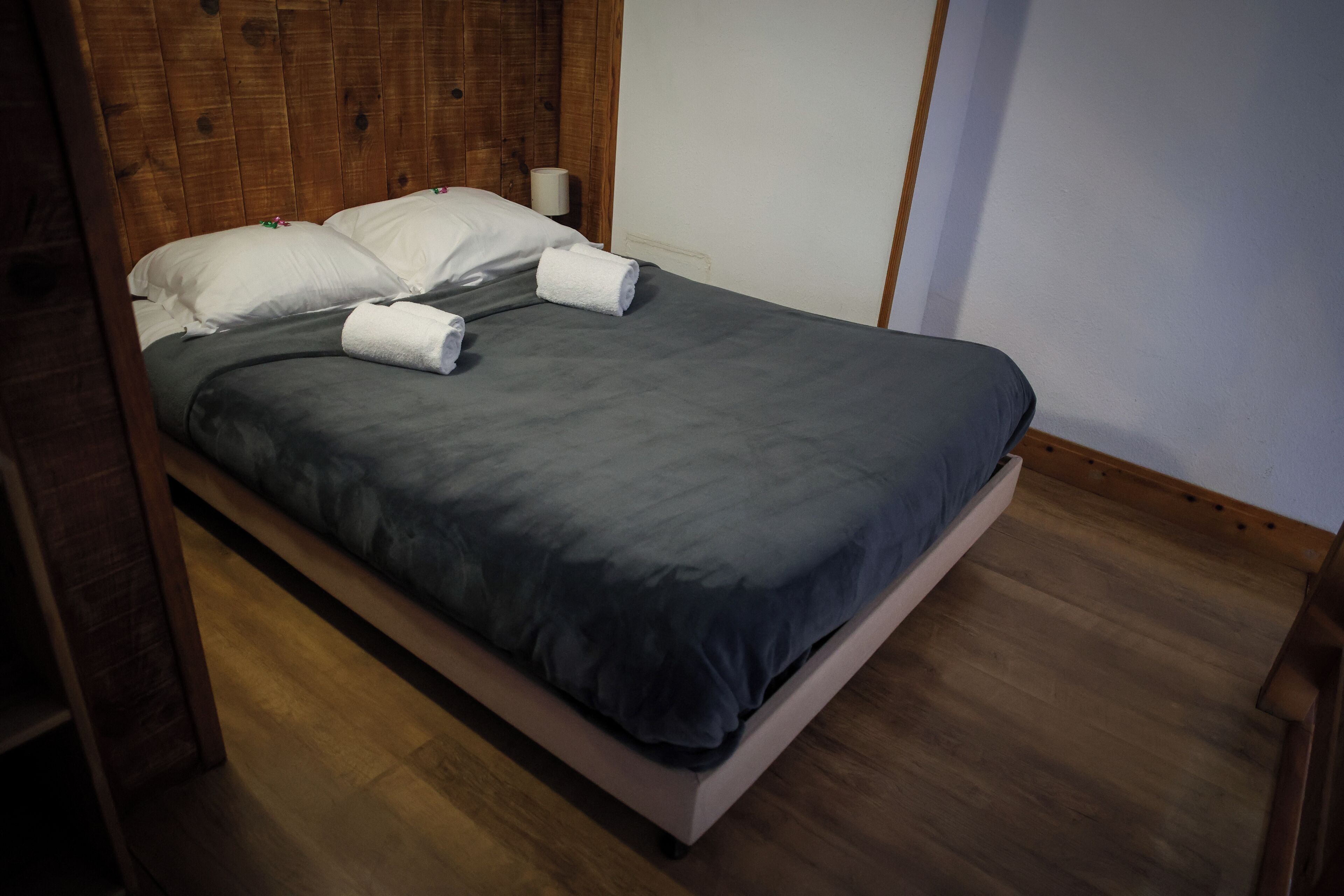 Un lit avec une couvre-lit grise, des oreillers blancs et deux serviettes enroulées.