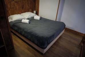 Un letto con una coperta grigia, cuscini bianchi e due asciugamani arrotolati.