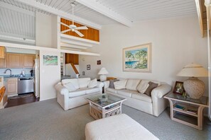 Ein modernes Wohnzimmer mit einem weißen Sofa, einem Glastisch und einem Deckenventilator.