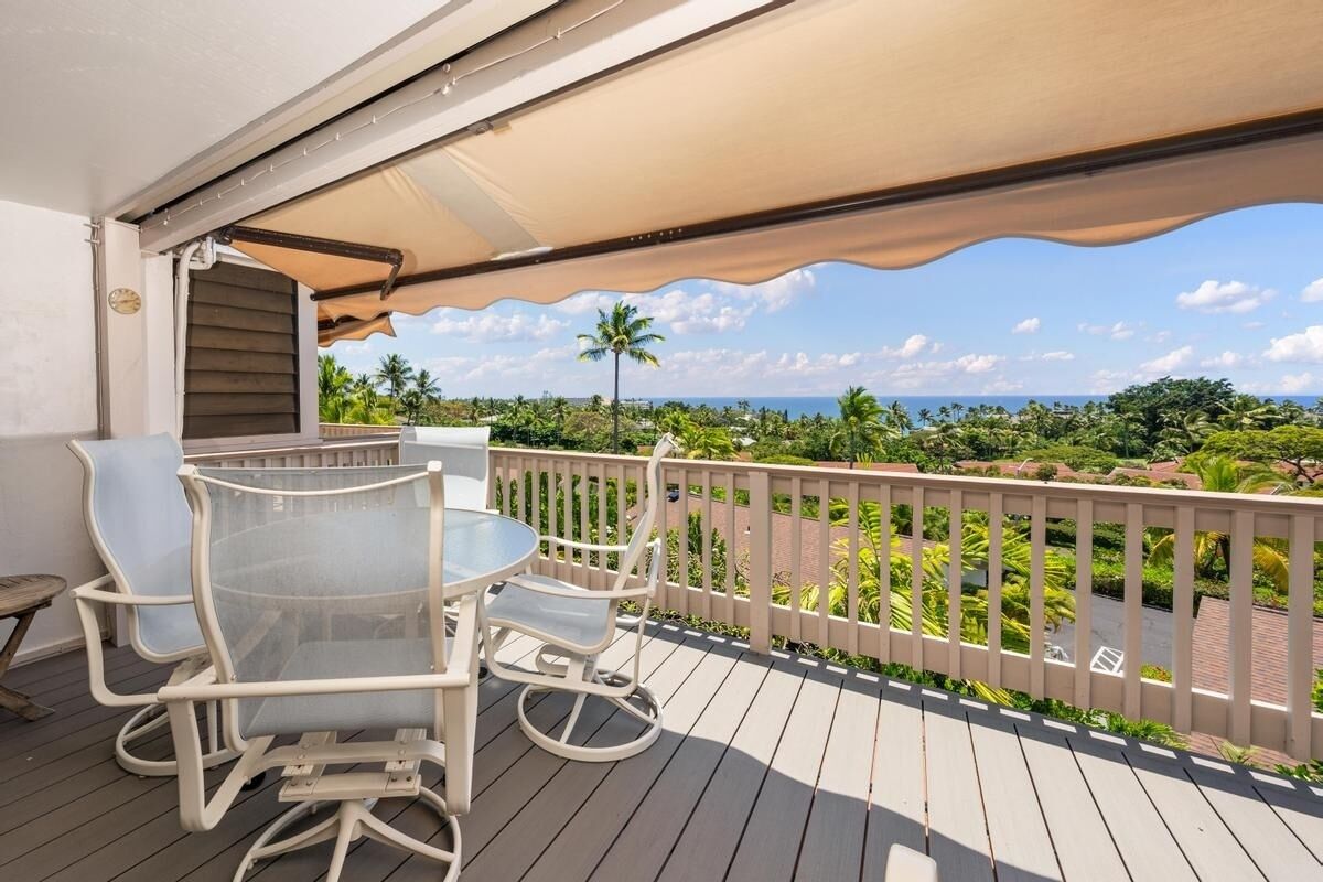 Ein Balkon mit Tisch und Stühlen, Blick auf den Ozean und eine Palme.