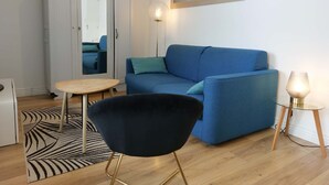 Un soggiorno moderno con un divano blu, una poltrona nera, un tavolino rotondo, un'armadio bianco e uno specchio sulla parete.