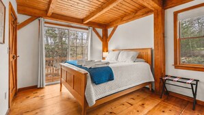 Une chambre avec un lit en bois, une fenêtre donnant sur des arbres et un plafond en bois.