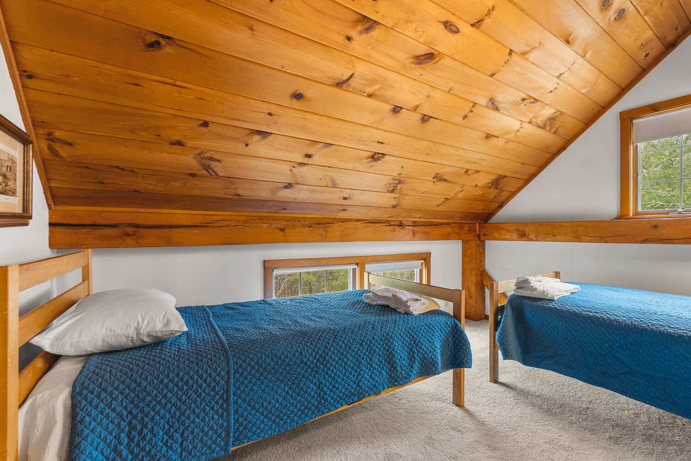 Une chambre avec deux lits, des poutres apparentes en bois au plafond et une fenêtre donnant sur la forêt.