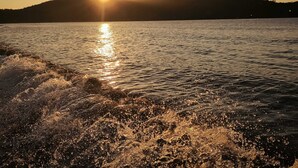 A sunset over a body of water with waves crashing onto a rocky shore.