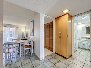Ein Zimmer mit Esstisch, Stühlen, einem Holzschrank, einem Badezimmer mit Spiegel und Waschbecken sowie einem Fenster mit Vorhängen.