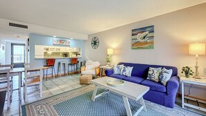 Ein Wohnzimmer mit blauem Sofa, einem Couchtisch und einer Küchenzeile mit Sitzhocker.