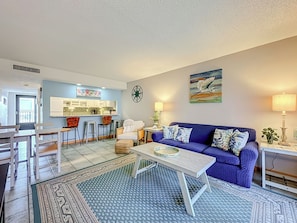 Ein Wohnzimmer mit blauem Sofa, einem Couchtisch und einer Küchenzeile mit Sitzhocker.