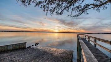 Un muelle de madera que se adentra en aguas tranquilas, con un atardecer de fondo.
