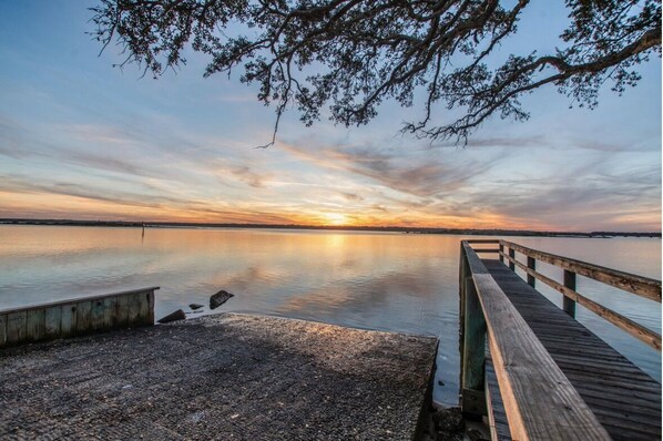 Eine Holzsteg, der in ruhiges Wasser führt, mit einem Sonnenuntergang im Hintergrund.