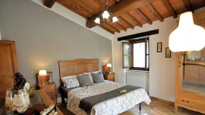 Een slaapkamer met een houten hoofdbord, een bed met een bloemenbedekking, twee bedlampen, een nachtkastje van hout, een kast en een raam met jaloezieën.