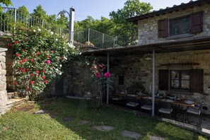 Ein Steingebäude mit Terrasse, Sitzgelegenheiten im Freien und einem Garten mit blühenden Pflanzen.