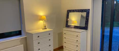 Quarto com uma cama, cômoda, espelho e janela.