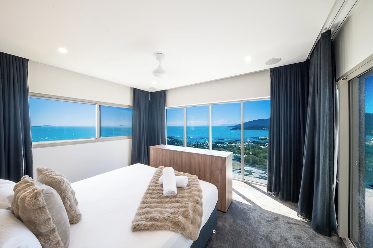 A hotel room with a large bed, a wooden nightstand, and a view of the sea.