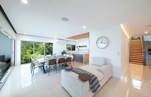 A modern living space with a dining area, kitchen, and a large window offering a view of greenery.