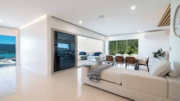 A modern living room with a sofa, dining table, and chairs. There is a large window with a view of the outdoors.