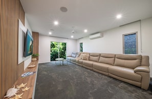 A modern living room with a beige sofa, a wooden accent wall, and a large window with a view of greenery.