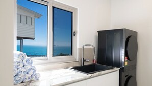 A kitchen with a sink, a black refrigerator, and a view of the ocean through a window. - Veduta Tal-Marina (Airlie Beach)