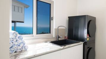 A kitchen with a sink, a black refrigerator, and a view of the ocean through a window.