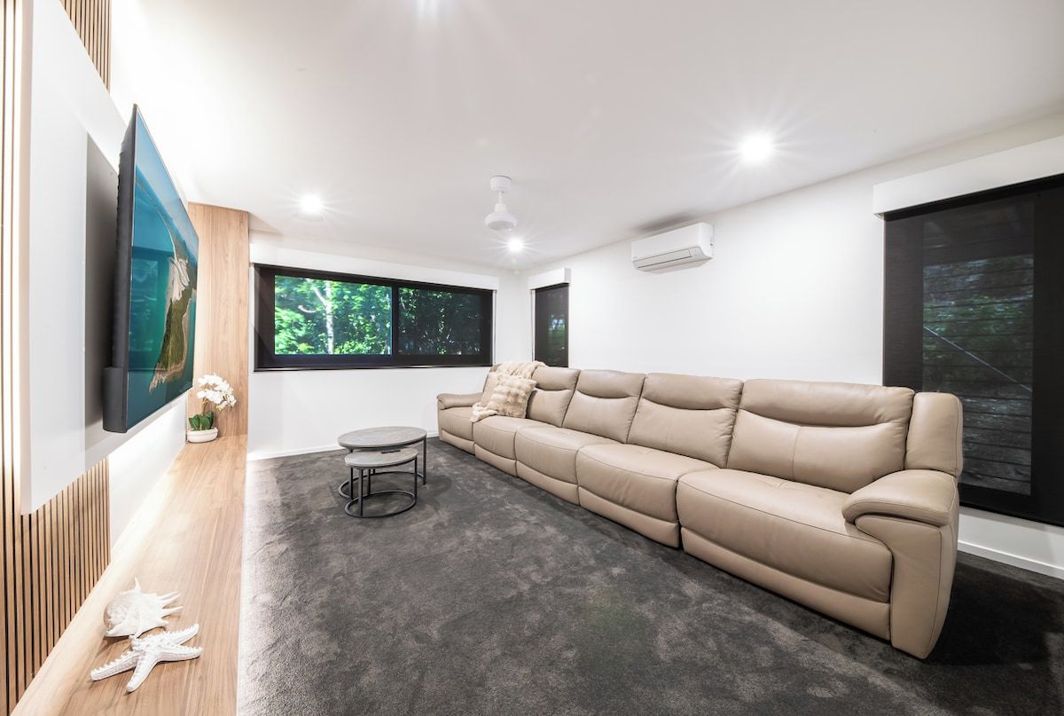 A modern living room with a beige sofa, a round coffee table, and a flat-screen TV mounted on the wall.