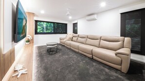 A modern living room with a beige sofa, a round coffee table, and a flat-screen TV mounted on the wall. - Veduta Tal-Marina (Airlie Beach)