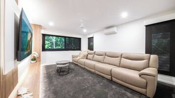 A modern living room with a beige sofa, a round coffee table, and a flat-screen TV mounted on the wall.