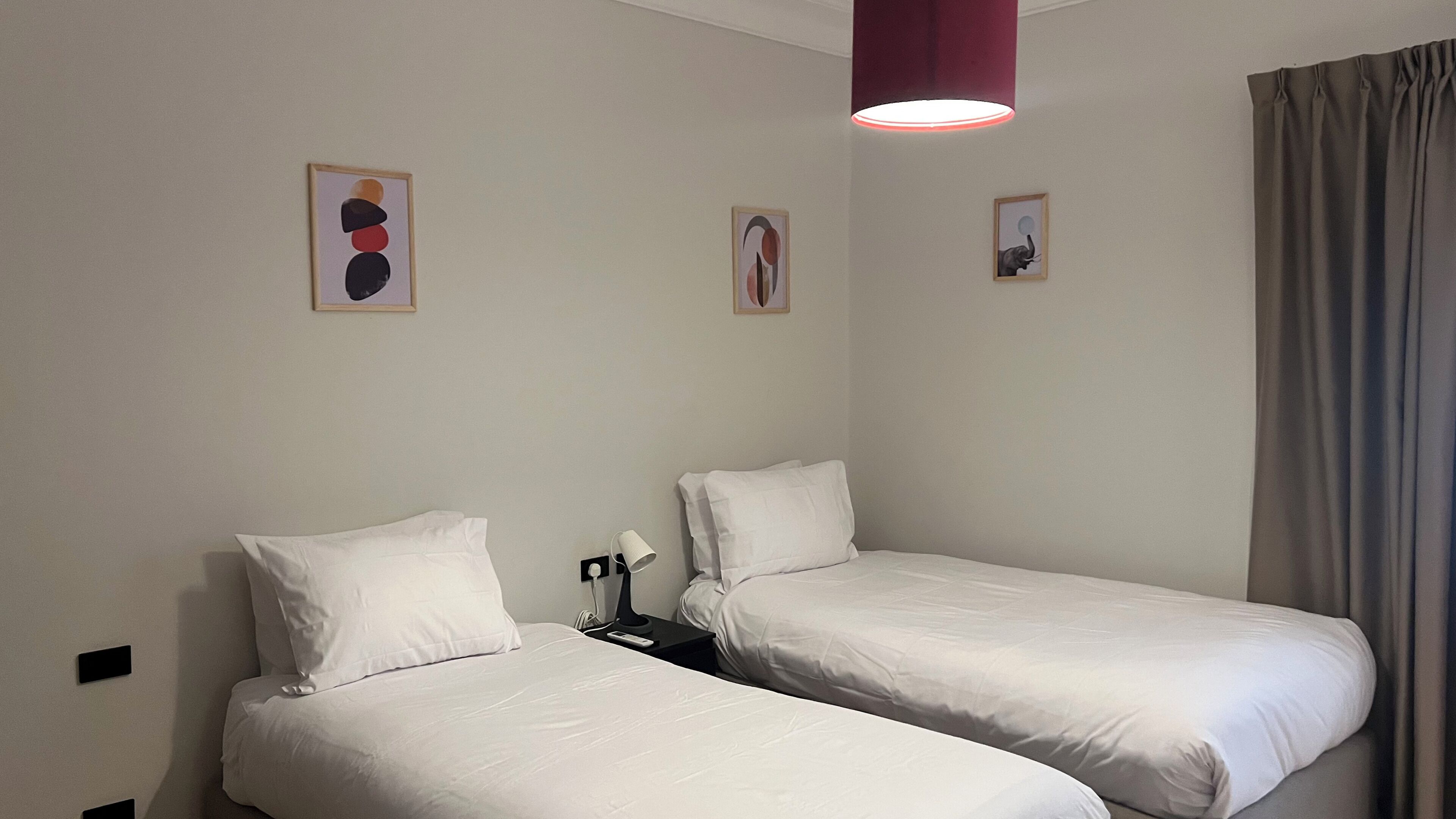 Una habitación de hotel con dos camas individuales, una mesita de noche con lámpara y una lámpara de techo roja.