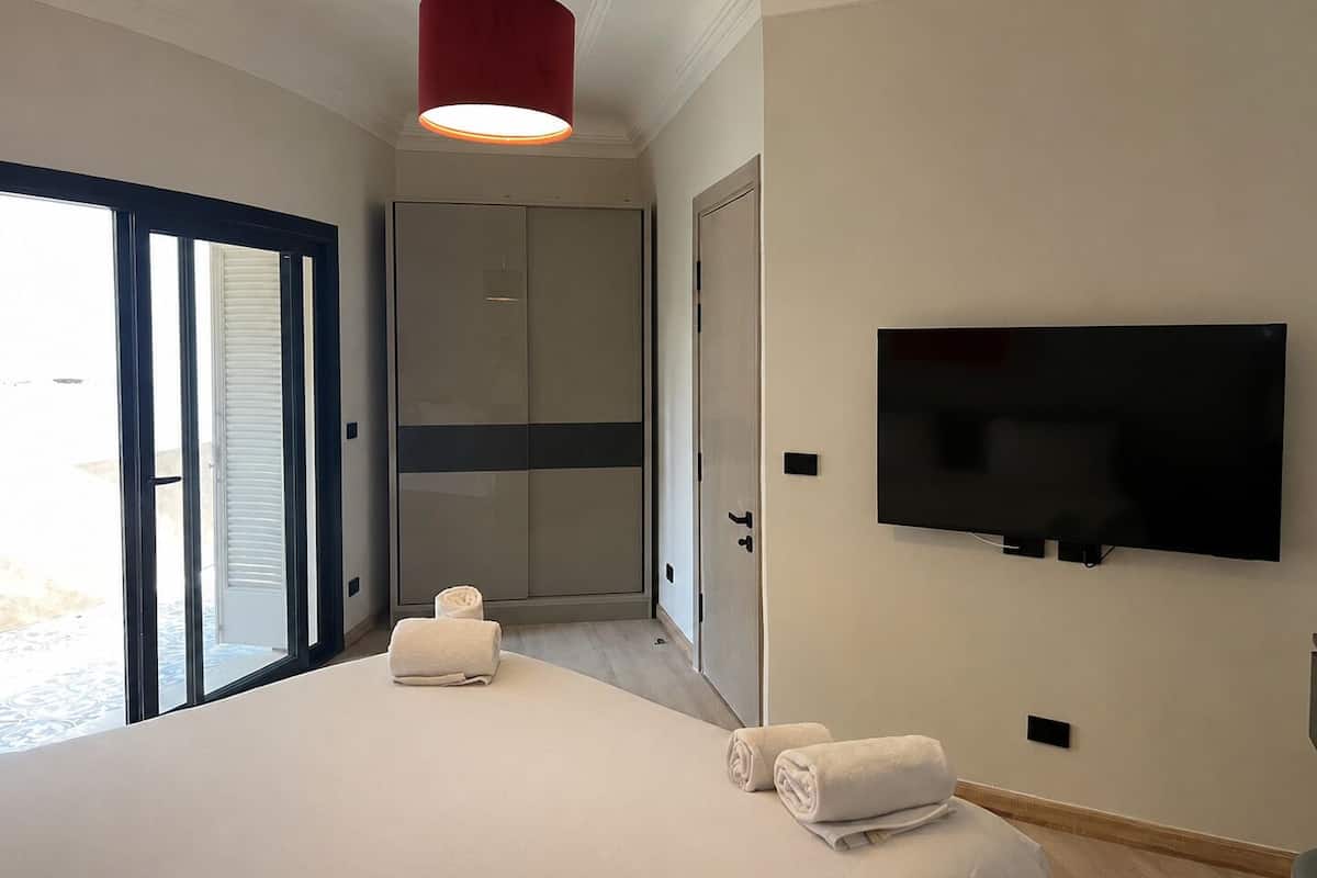 Ein Hotelzimmer mit einem Bett, einem an der Wand montierten Fernseher, einer Schiebetür und einer roten Pendelleuchte.