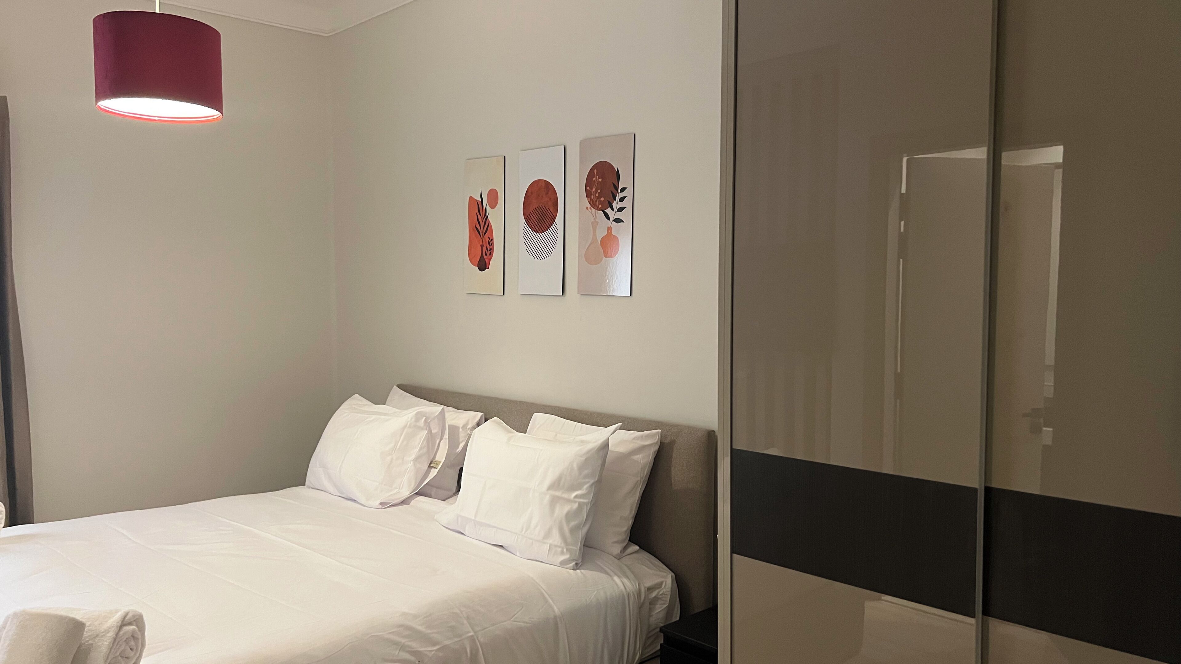 Une chambre d’hôtel avec un lit, un lampadaire suspendu rouge et trois œuvres d’art murales.